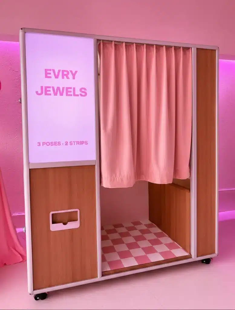 Custom EVRY JEWELS enclosed photo booth setup with pink branding, satin curtain, and wood panels for a brand activation.