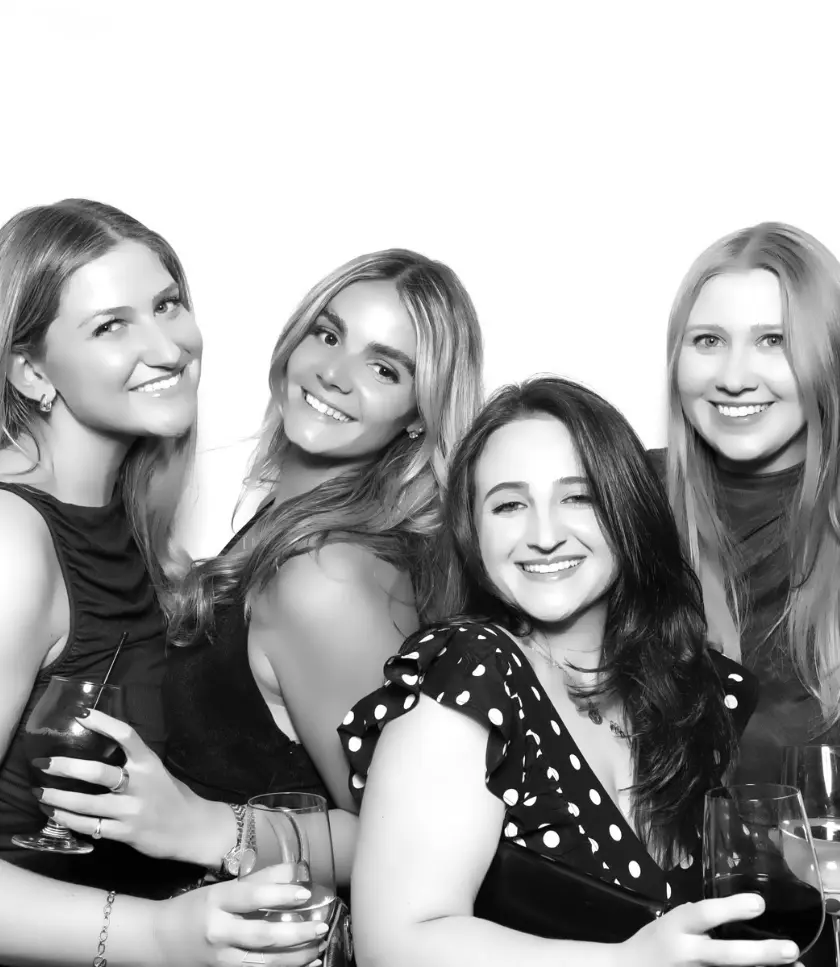 Four people smiling and holding drinks in a photo booth.