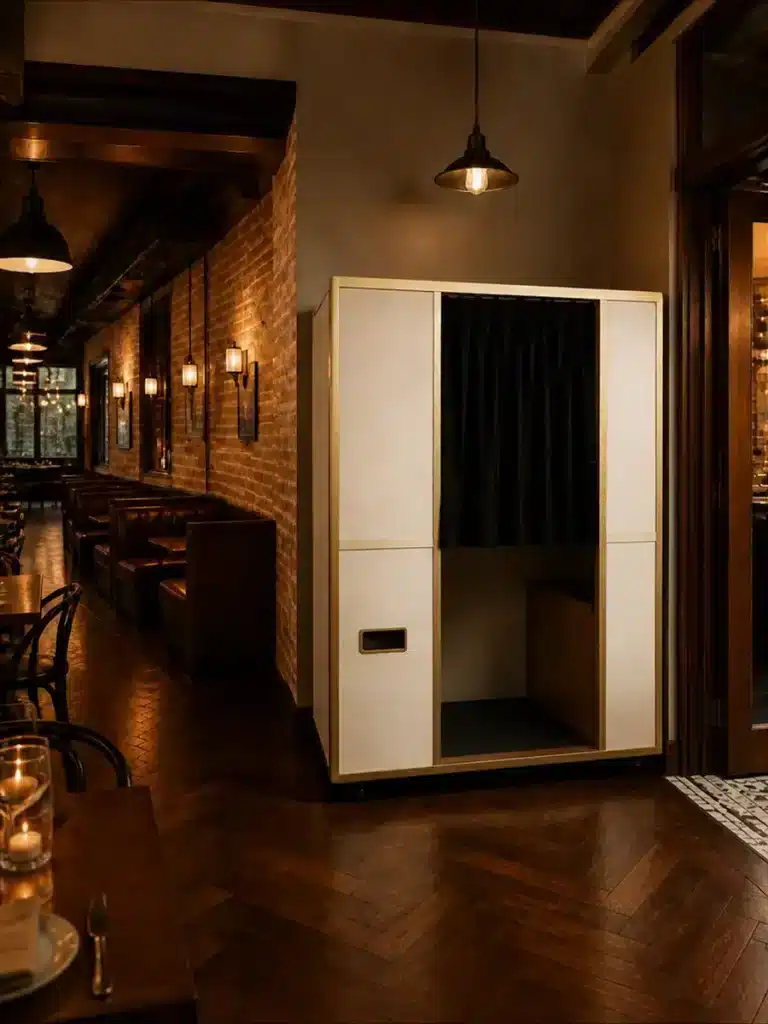 An enclosed photo booth with a black curtain stands in a restaurant with booth seating and brick walls.