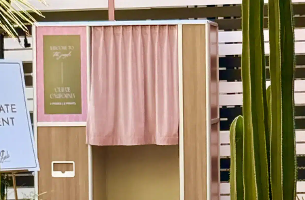 enclosed photo booth with a pink curtain set up outdoors beside a tall cactus.