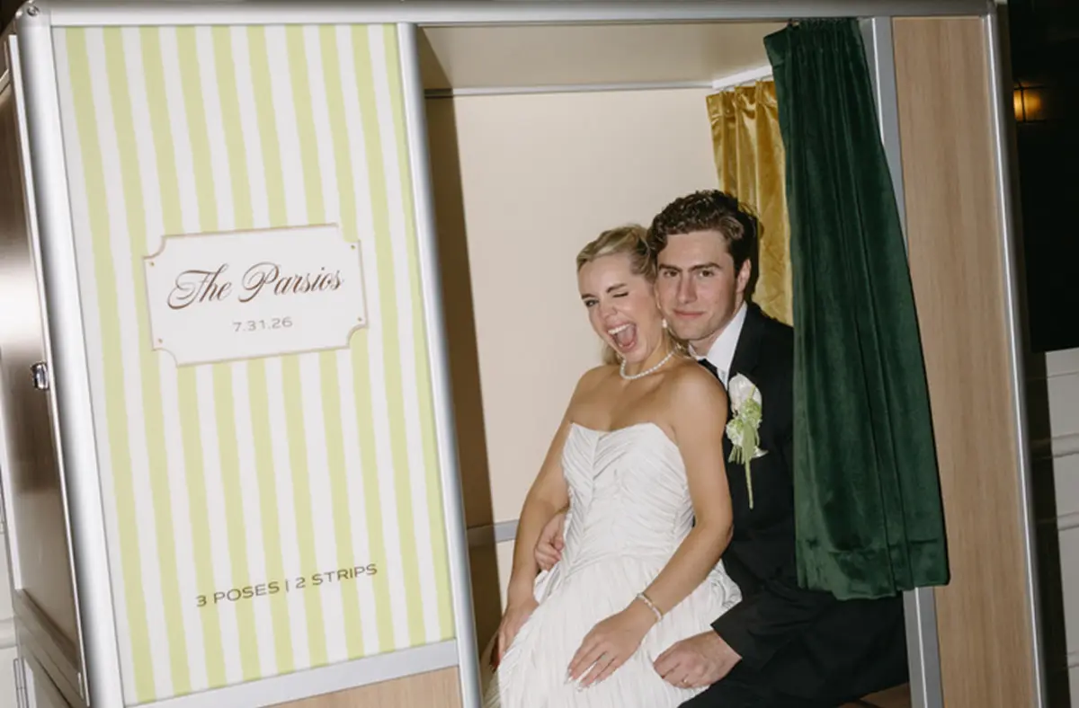 a couple pose together inside a wooden enclosed photo booth at their wedding