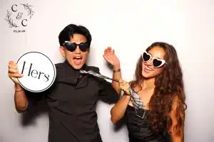 Couple wearing heart sunglasses, laughing with props in a fun photo booth portrait.