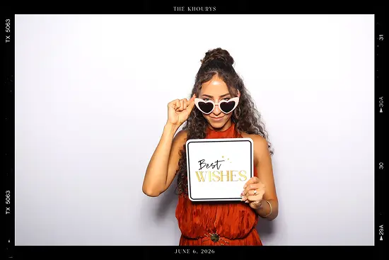 Woman wears heart-shaped sunglasses and holds a “Best Wishes” sign