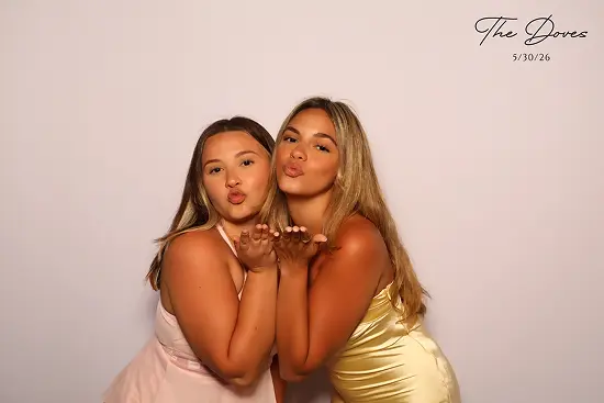 Two women lean together and blow kisses toward the camera