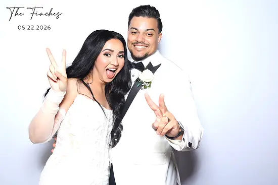 Bride and groom smile while holding up peace signs in a playful wedding photo booth pose.