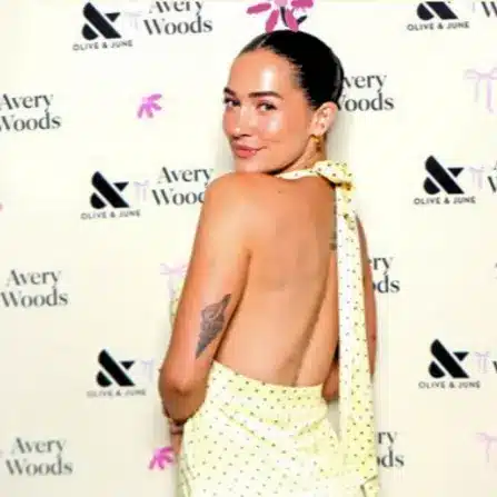 Guest posing in a backless, light yellow polka-dot dress in front of a custom Avery Woods x Olive & June branded photo booth backdrop featuring both logos.
